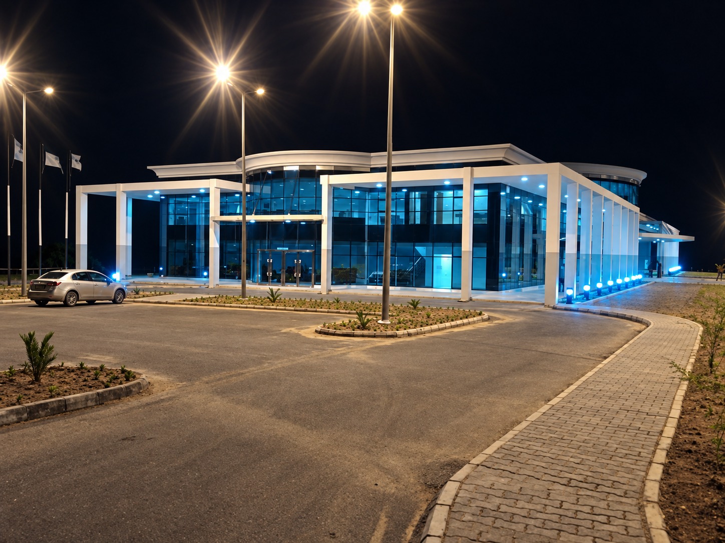 Night view of the airport terminal entrance with lit glass facade, flags and roadway